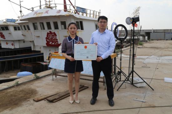 海鮮電商張夢琴與幫辦員手持食品經(jīng)營許可證合影。贛榆區(qū)委宣傳部供圖