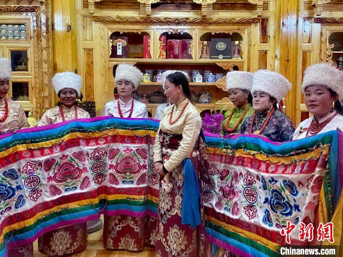 圖為女性展示村民自發(fā)繡制的“百米五彩哈達(dá)”。　李玉峰 攝
